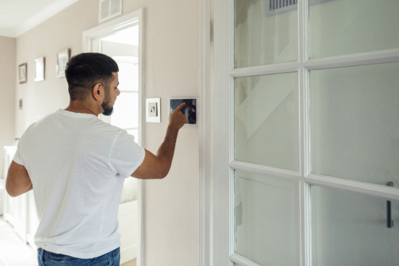 Does Turning the Heat On and Off Save Money? A man using a smart thermostat turning the heat back on.