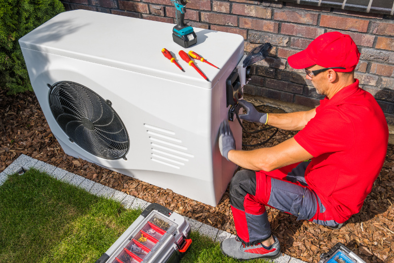 4 Factors to Consider When Buying a Heat Pump. A repairman fixing a heat pump outside of a home.