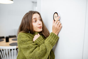 Why Is My Heat Pump Turning On and Off Frequently? A woman turning up her thermostat.